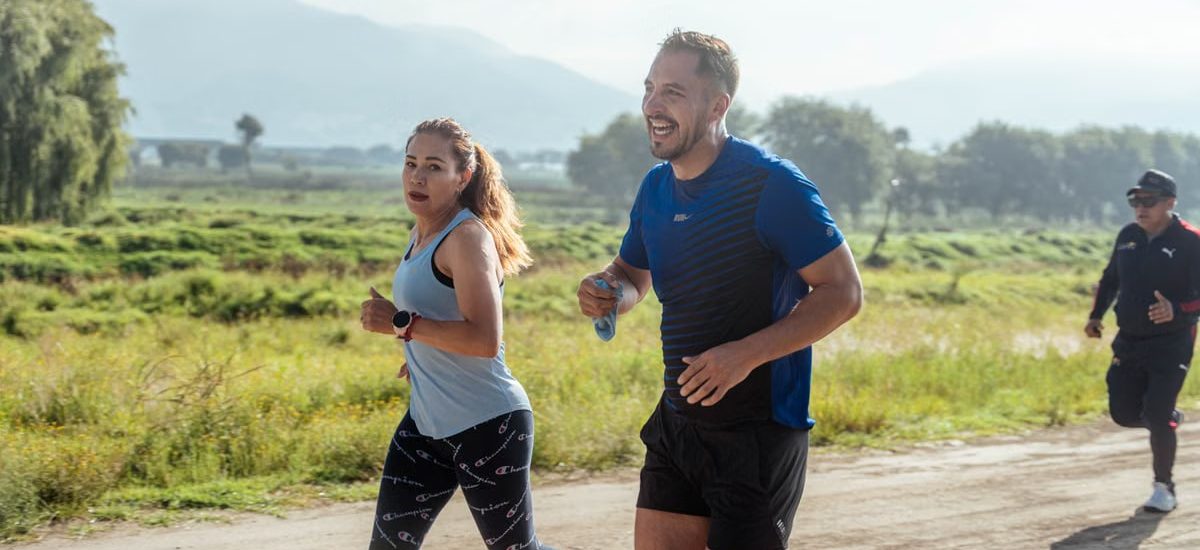 Two adults running on a rural dirt path, enjoying a sunny day outdoors.