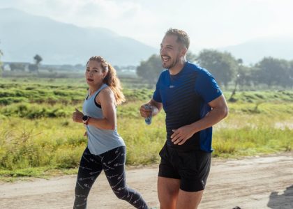 Two adults running on a rural dirt path, enjoying a sunny day outdoors.